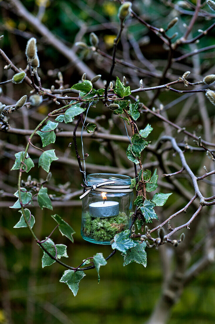 Entzündetes Teelicht in einem Marmeladenglas mit Moos und natürlichem Efeukranz in einem Londoner Garten, England, UK