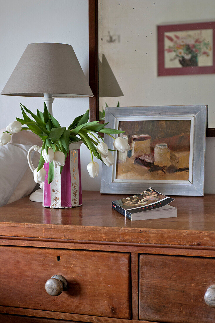 Weiße Tulpen und ein Taschenbuch auf einer Holzkommode in einem Strandhaus in Cornwall England UK