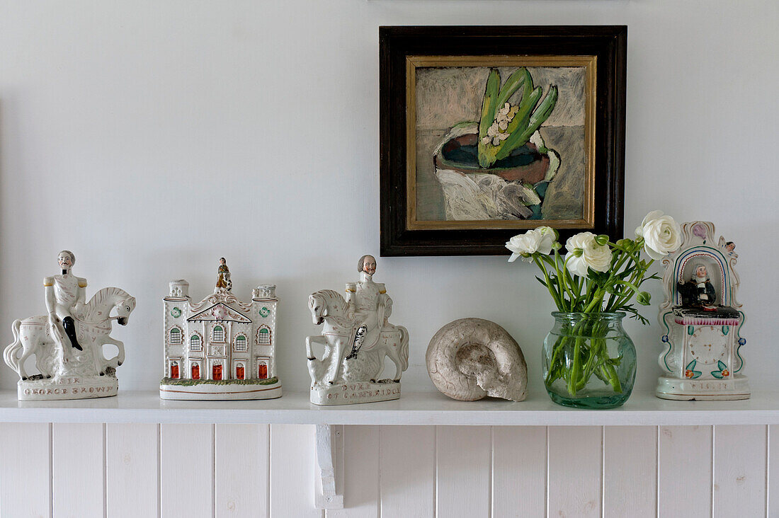Camellias and figurines with framed artwork on bathroom shelf in beach house Cornwall England UK