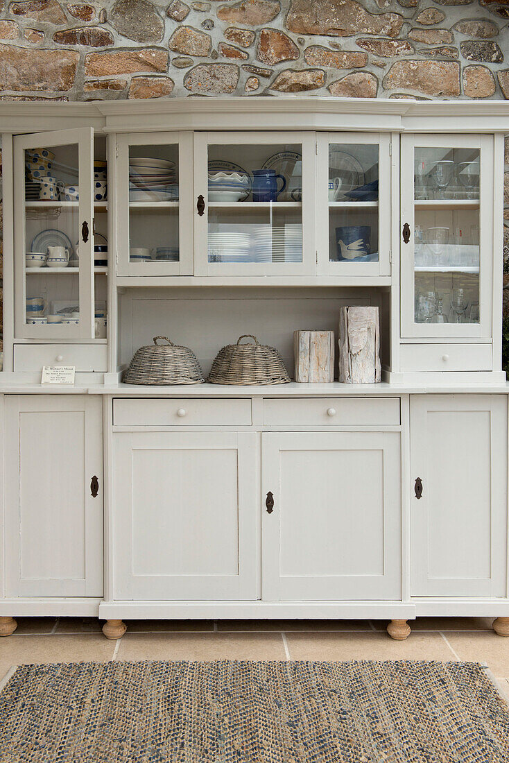 Cream kitchen dresser with exposed stone wall in Penzance farmhouse Cornwall England UK