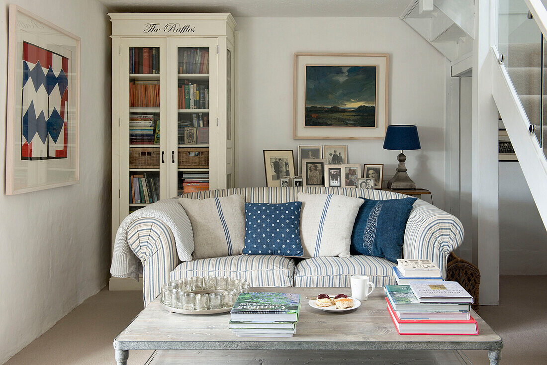 Familienfotos mit Bücherregal mit Glasfront und Sofa im Wohnzimmer eines Bauernhauses in Penzance, Cornwall, England UK