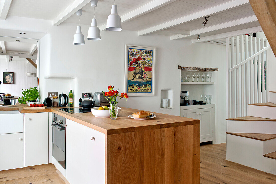 red freesias on wooden island unit in open plan stucco kitchen of family townhouse Cornwall England UK