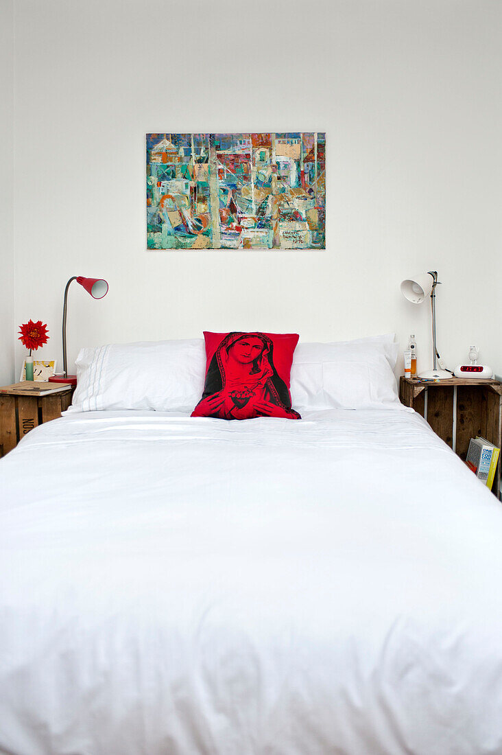 Artwork above double bed with side lamps and cushion with religious icon in townhouse bedroom Cornwall England UK