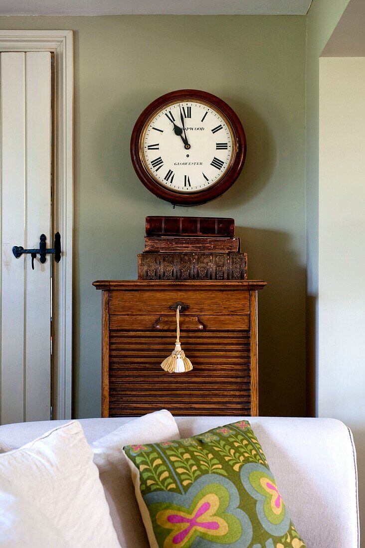 Clock above vintage wooden cabinet and sofa with cushion in Edworth living room Bedfordshire England UK