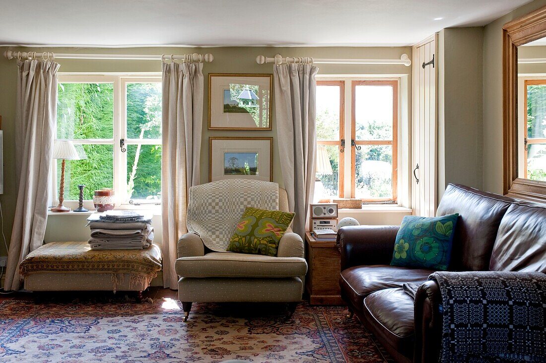 Cream armchair with brown leather sofa in living room of Edworth cottage Bedfordshire England UK
