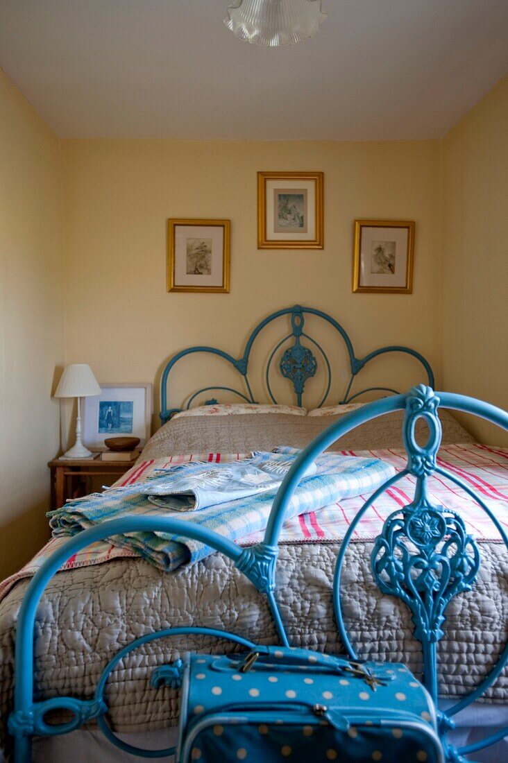 Blue painted metal bed with gilt framed artwork in Edworth cottage Bedfordshire England UK
