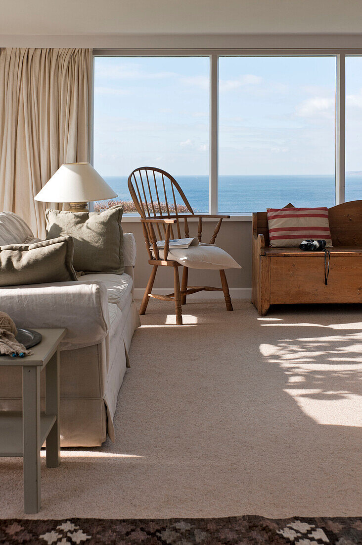 Holzstuhl und Deckenkiste mit Sofa am Panoramafenster eines Strandhauses in Cornwall, England UK