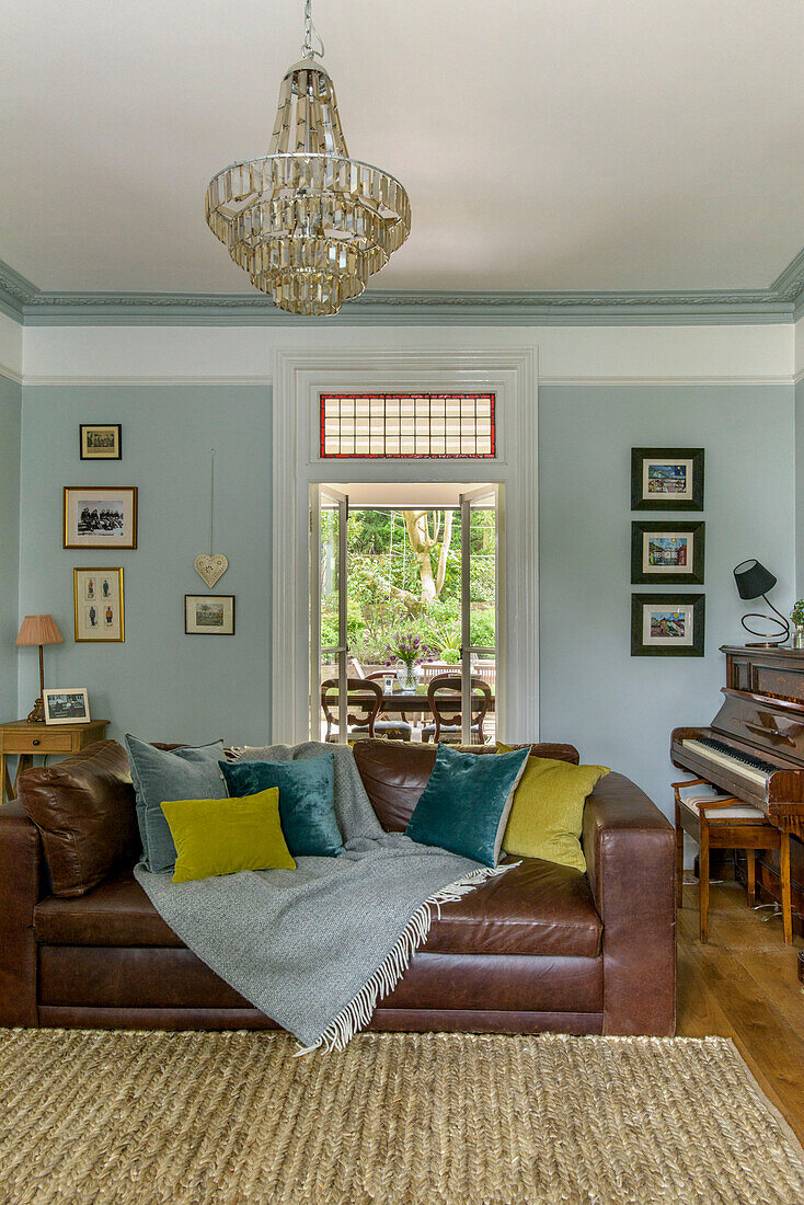 Braunes Ledersofa in hellblauem Wohnzimmer mit Glaslüster und Klavier in einem Einfamilienhaus in Tunbridge Wells, Kent, England, UK