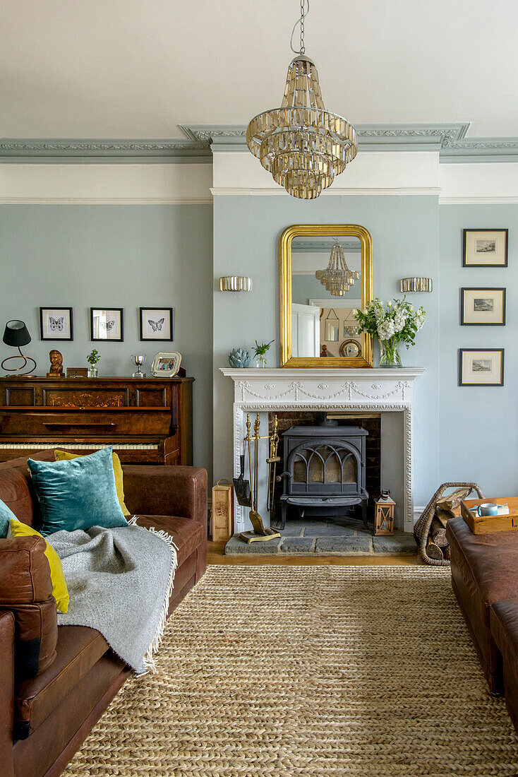 Braunes Ledersofa in einem hellblauen Wohnzimmer mit Glaslüster und Holzofen in einem Einfamilienhaus in Tunbridge Wells, Kent, England, UK