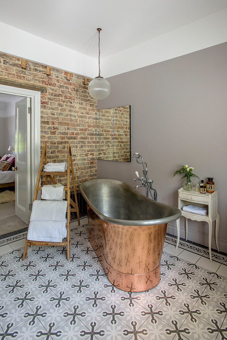 Kupferbadewanne mit gefliestem Boden und freigelegter Ziegelwand im Badezimmer eines Hauses in Tunbridge Wells, Kent, England, UK