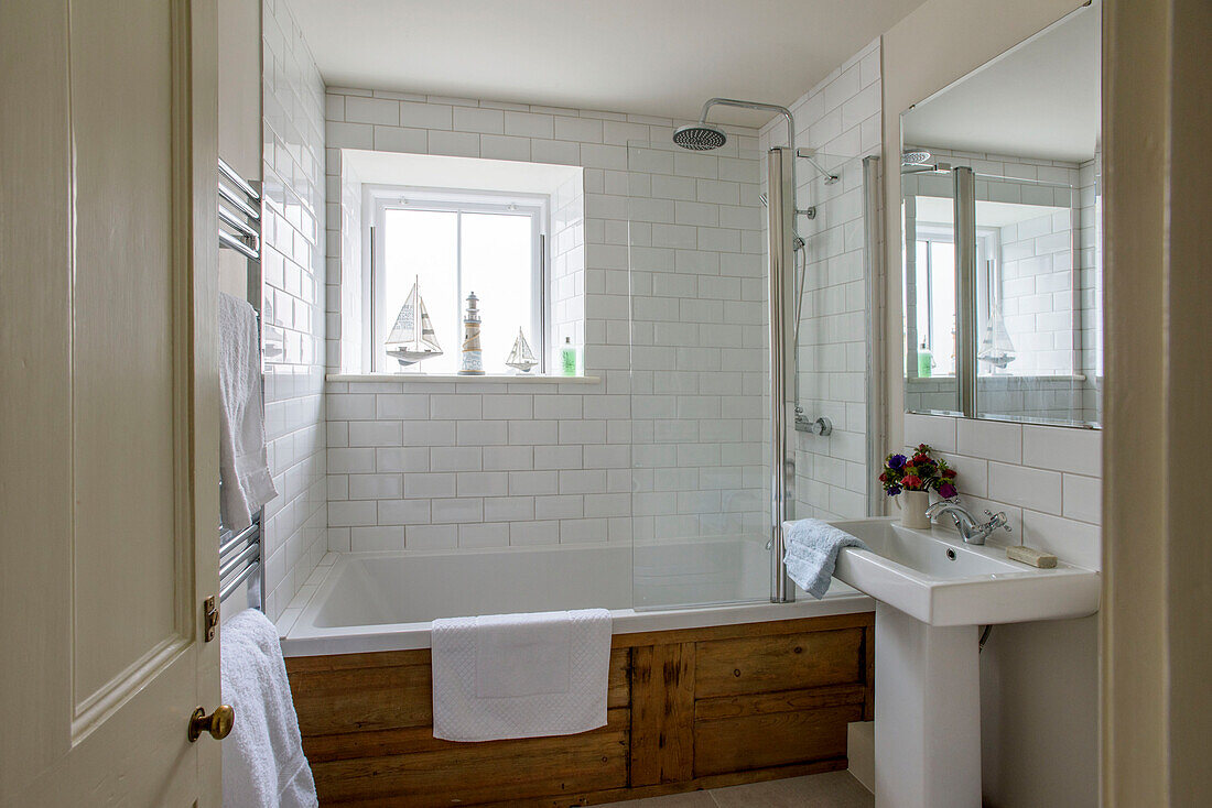 White tiled bathroom with wooden bath surround in St Ives home Cornwall UK
