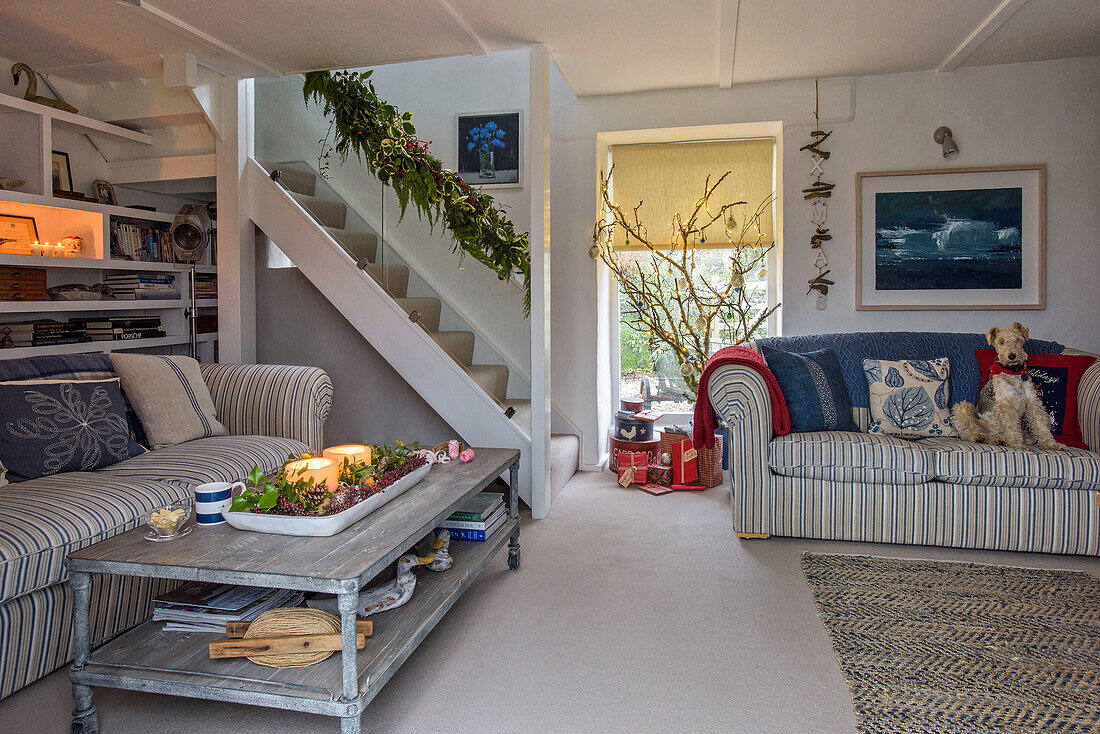 Lit candles on coffee table with striped sofas in open plan living room with staircase in Penzance farmhouse Cornwall UK