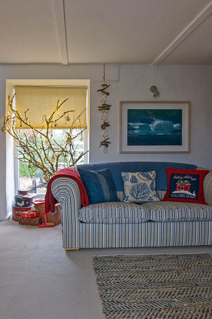 Gestreiftes Sofa mit blauer Decke unter gerahmtem Kunstwerk mit Weihnachtsdekoration in einem Bauernhaus in Penzance, Cornwall, Großbritannien
