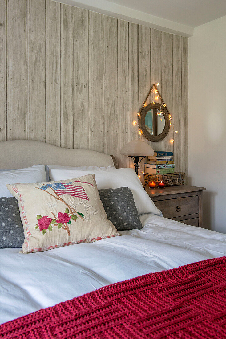 Circular mirror with fairylights above chest of drawers at bedside in Penzance farmhouse Cornwall UK