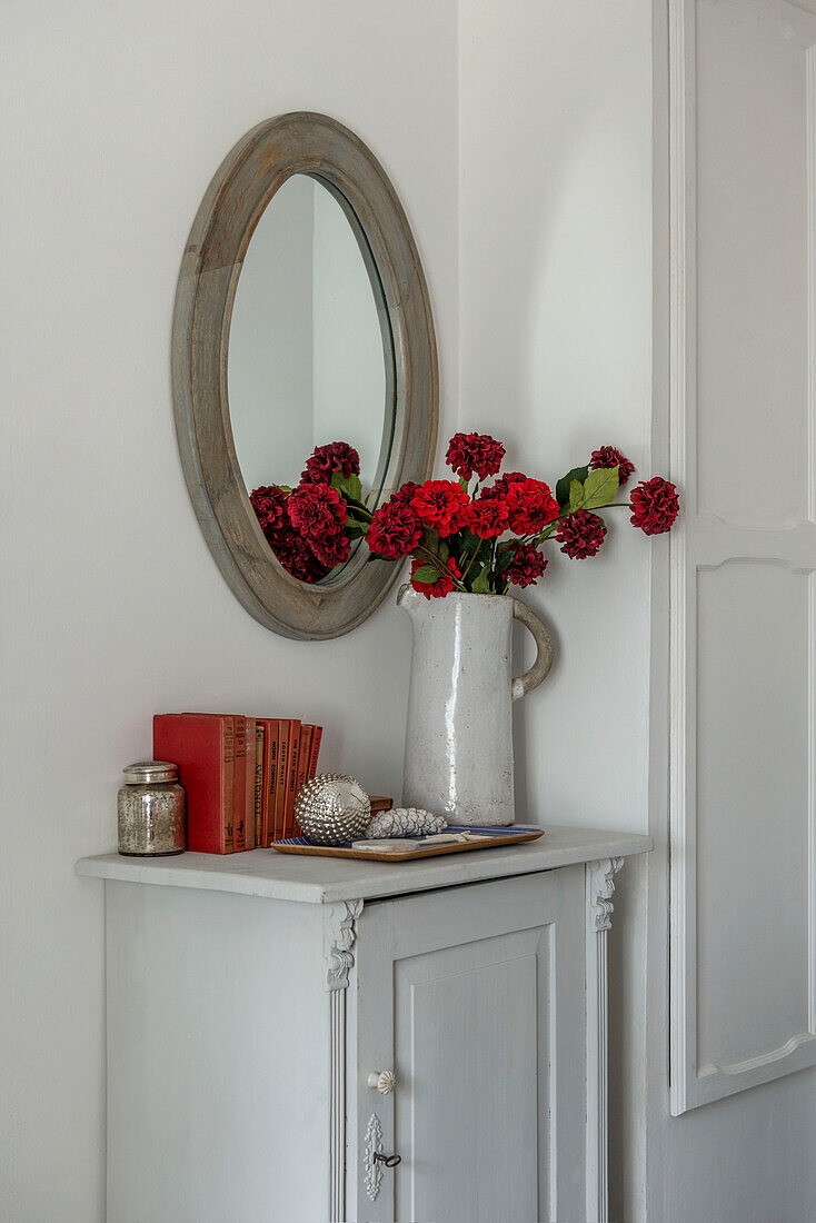 Ovaler Spiegel mit roten Schnittblumen in Keramikkanne in einem Bauernhaus in Penzance, Cornwall, UK