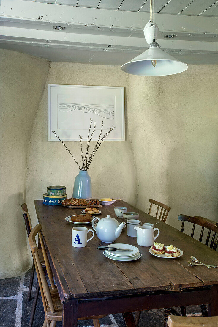 Wooden table below white pendant light with artwork set with scones for afternoon tea in Helston farmhouse Cornwall UK