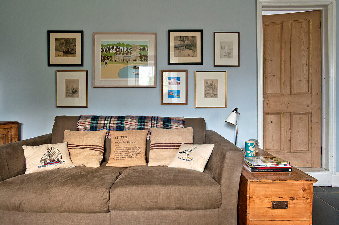 Kunstwerk-Display über braunem Sofa mit Kissen im Wohnzimmer eines Ferienhauses in Cornwall England