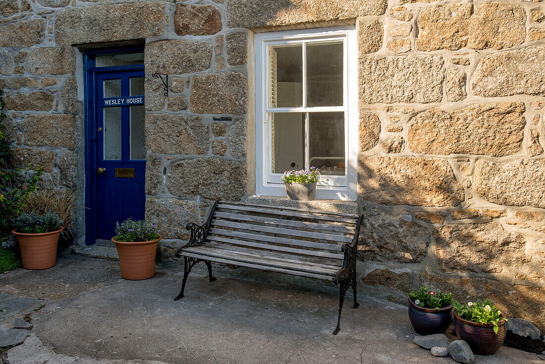 Sitzbank vor einem Cottage aus Stein mit blauer Eingangstür in Cornwall, Großbritannien