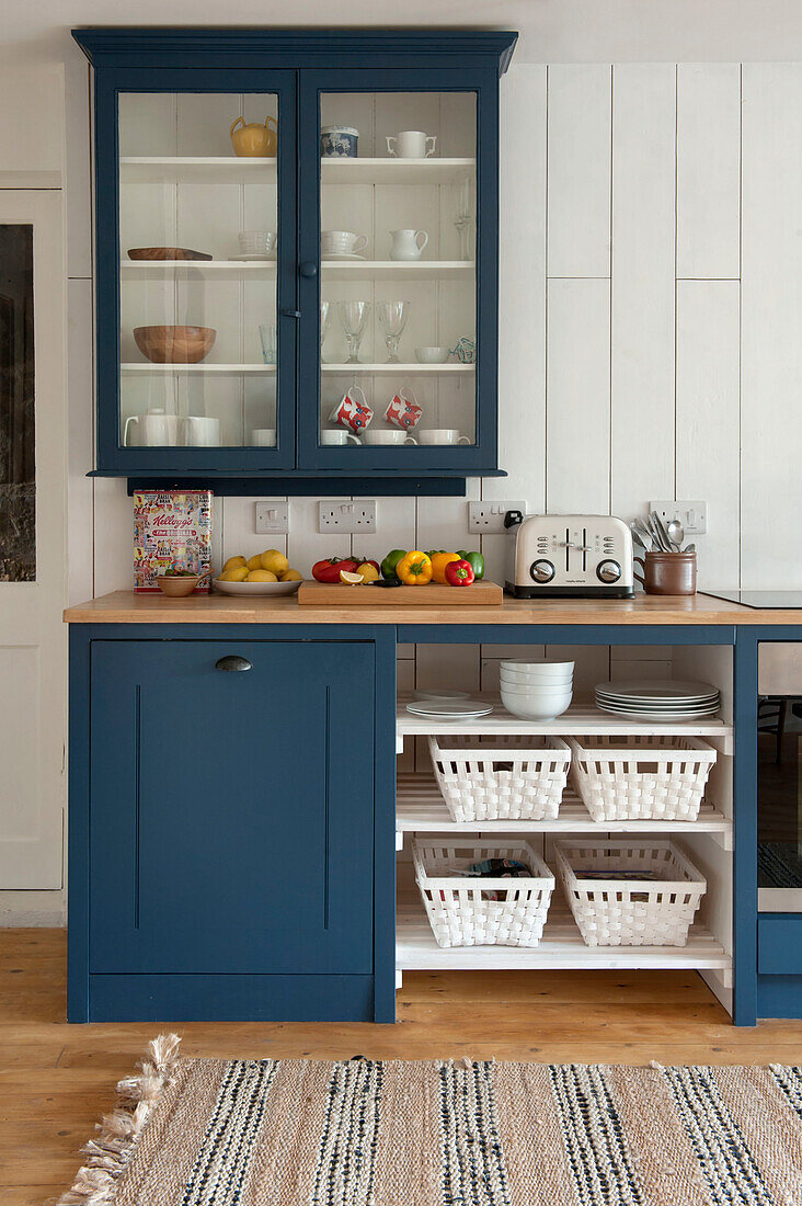 Glasschrank über der Arbeitsplatte mit blauem Anstrich in einer getäfelten Küche in einem Cottage in Cornwall (UK)