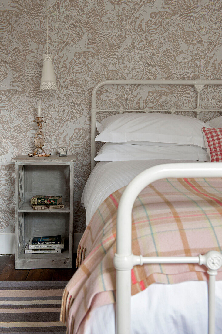 Schottenkaro-Decke auf einem Doppelbett mit gemusterter Tapete und Nachttisch Cornwall UK