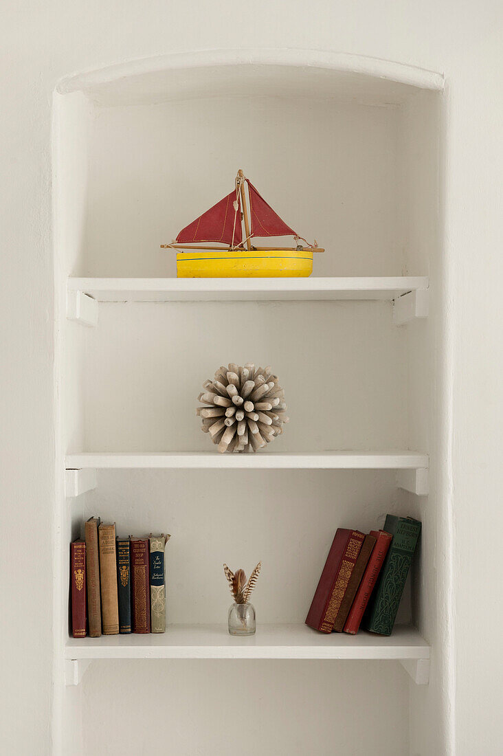 Spielzeugboot und gebundene Bücher in einem Nischenregal Cornwall UK