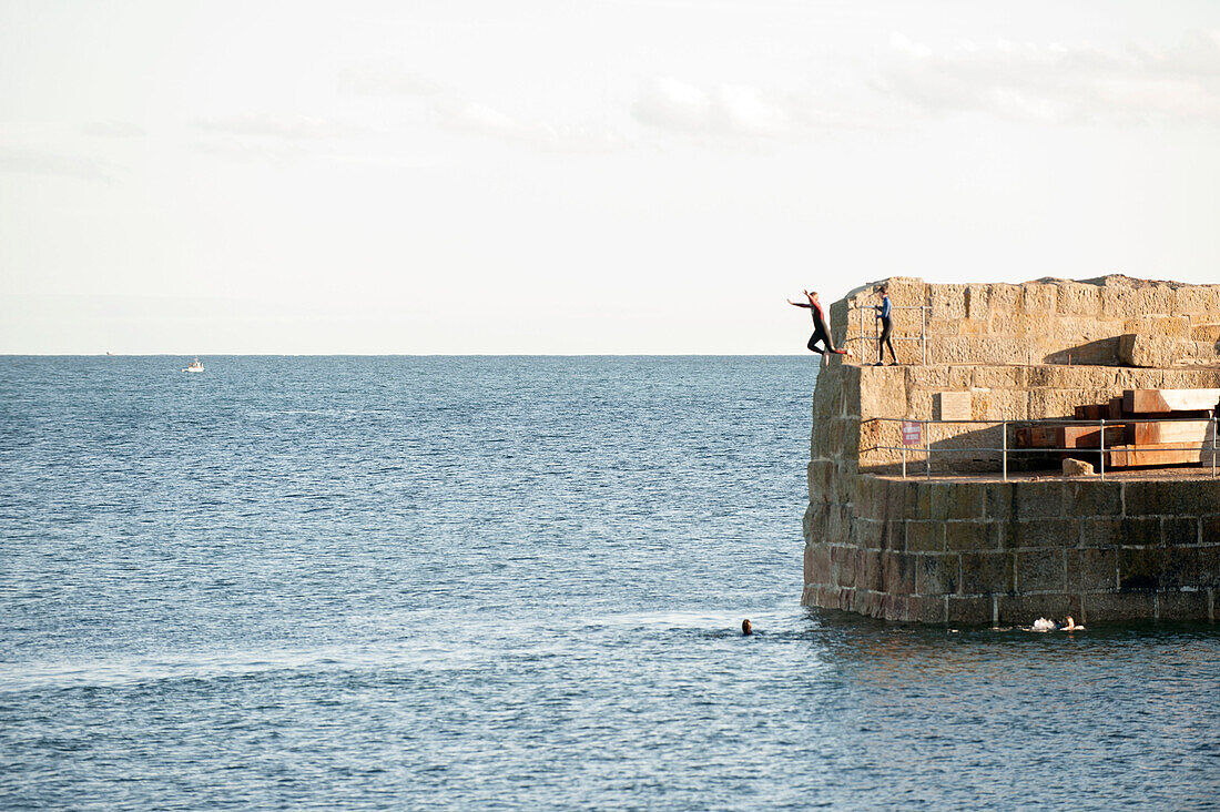 Kinder in Neoprenanzügen springen von der Hafenmauer Cornwall UK