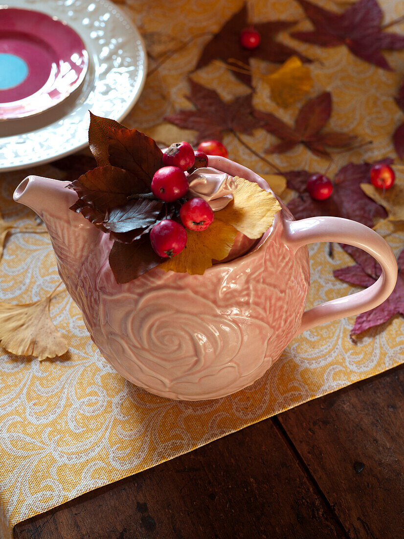 Beeren und Blätter in einer weißen Keramik-Teekanne auf einem hölzernen Esstisch in einem Haus im Vereinigten Königreich