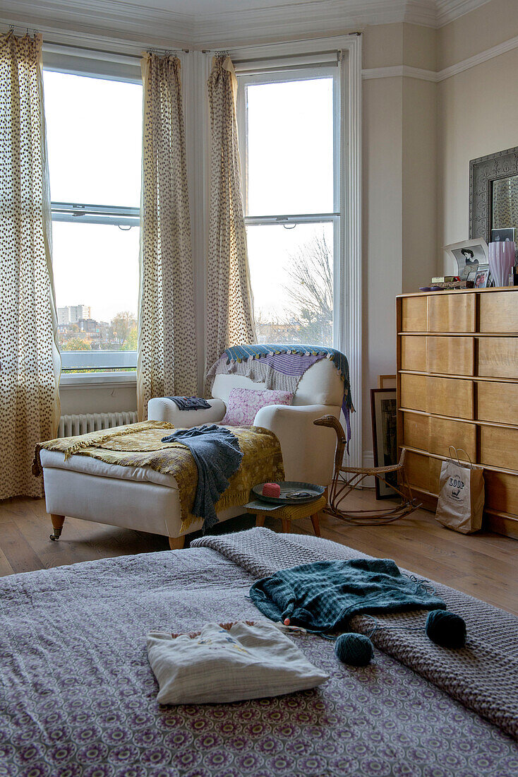 Stricken auf einem Doppelbett mit Sessel und Hocker in einem Erkerfenster in einem Haus in London, UK