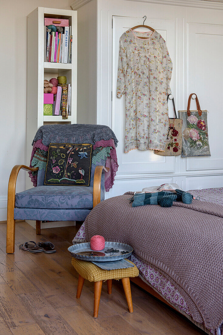 Sommerkleid und Taschen hängen an einem Kleiderschrank mit Sessel und Strickzeug in einem Londoner Schlafzimmer UK