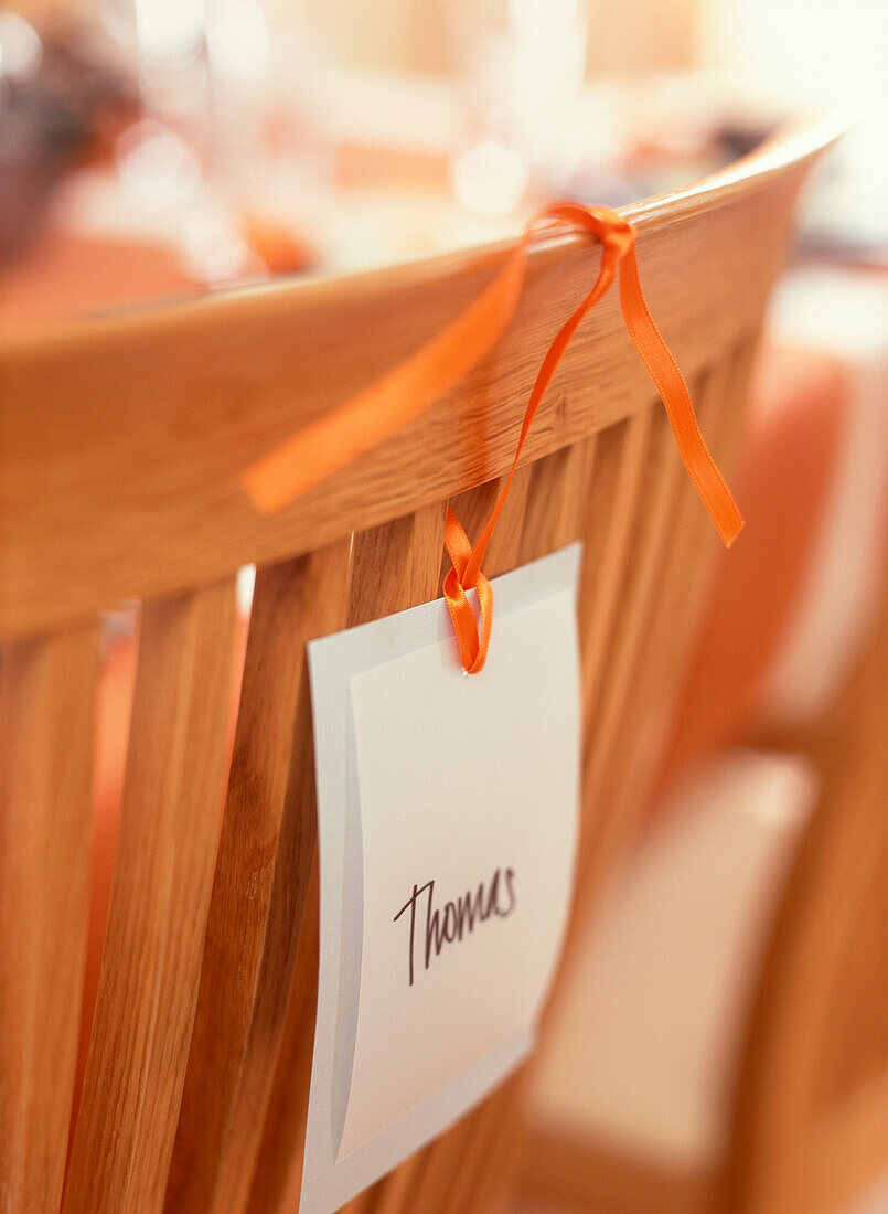 Name tag with Thomas tied to the back of a dining chair with orange ribbon