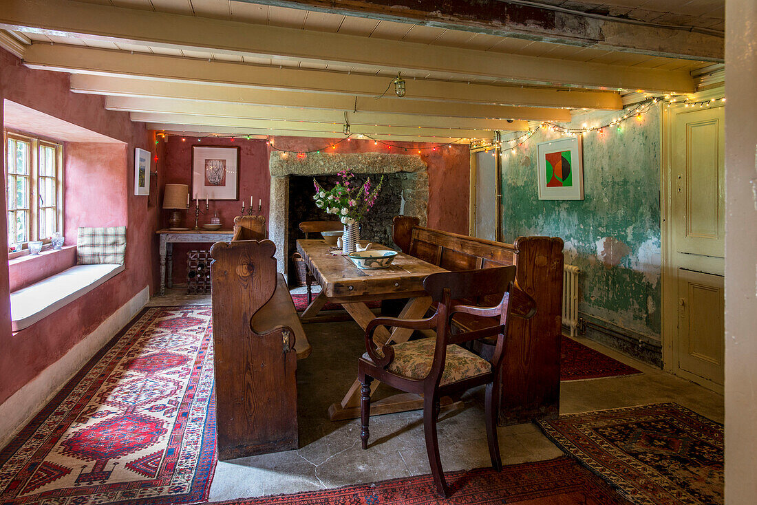 Altmodische Sitzbank und Tisch aus Holz mit gemusterten Teppichen in einem Bauernhaus in Helston, Cornwall UK