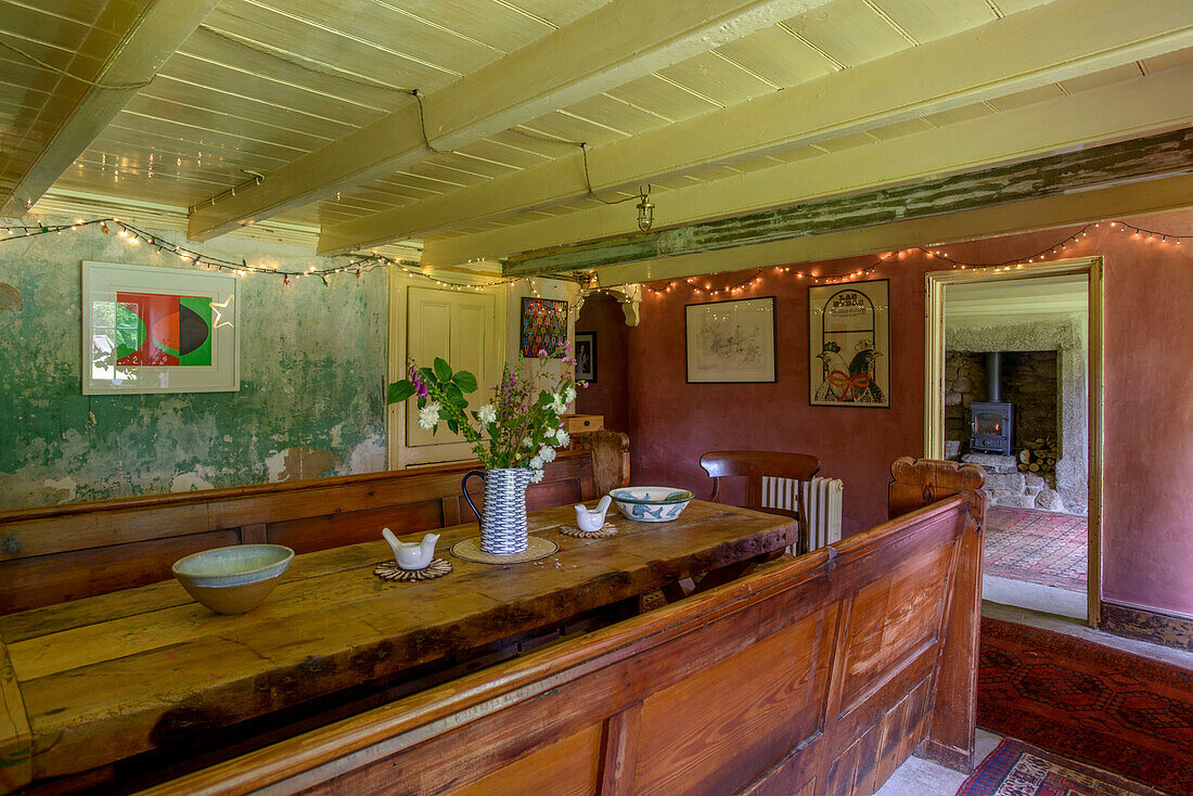 Altmodische Sitzbank und Tisch aus Holz mit beleuchteten Fenstern in einem Bauernhaus in Helston, Cornwall UK