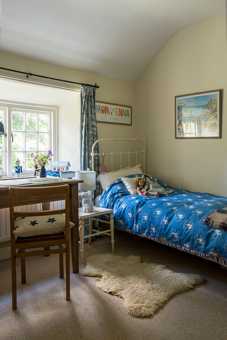 Blaue Bettdecke auf metallgerahmtem Einzelbett mit Schreibtisch und Stuhl am Fenster in einem Bauernhaus in Helston, Cornwall, Großbritannien