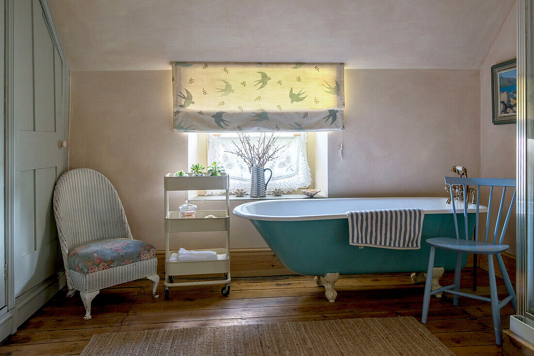 Freestanding turquoise bath with chairs and service trolley at window in Helston farmhouse Cornwall UK