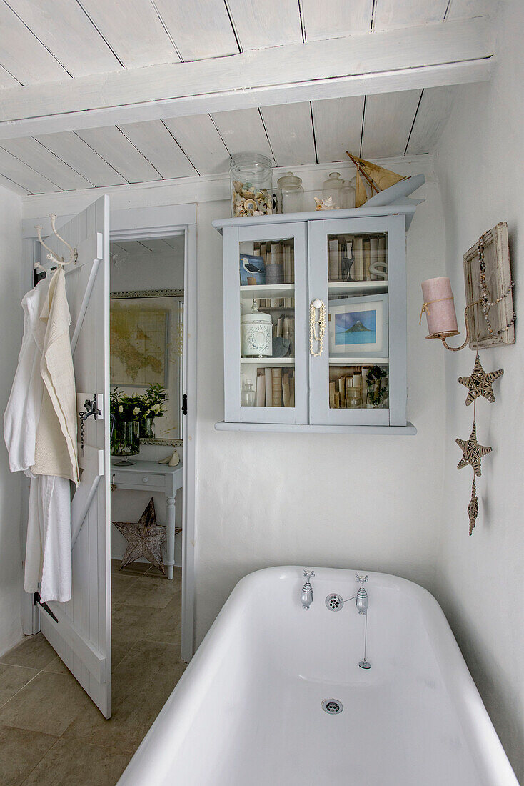 Glasschrank über einer freistehenden Badewanne in einem Strandhaus in Marazion, Cornwall, Großbritannien