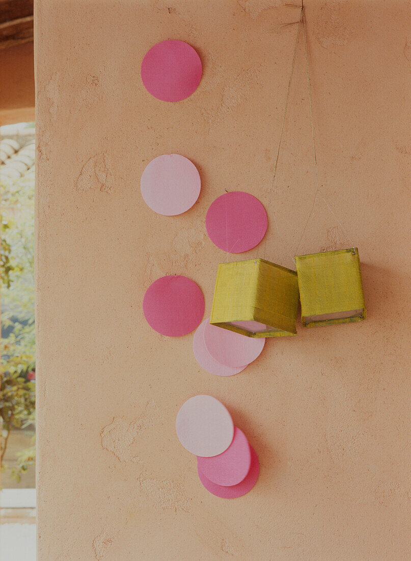Rosa Papierpunkte und grüne Laternen vor einer grob verputzten Wand