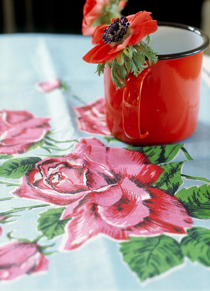 Red anenome in enamel mug on flower print tablecloth 