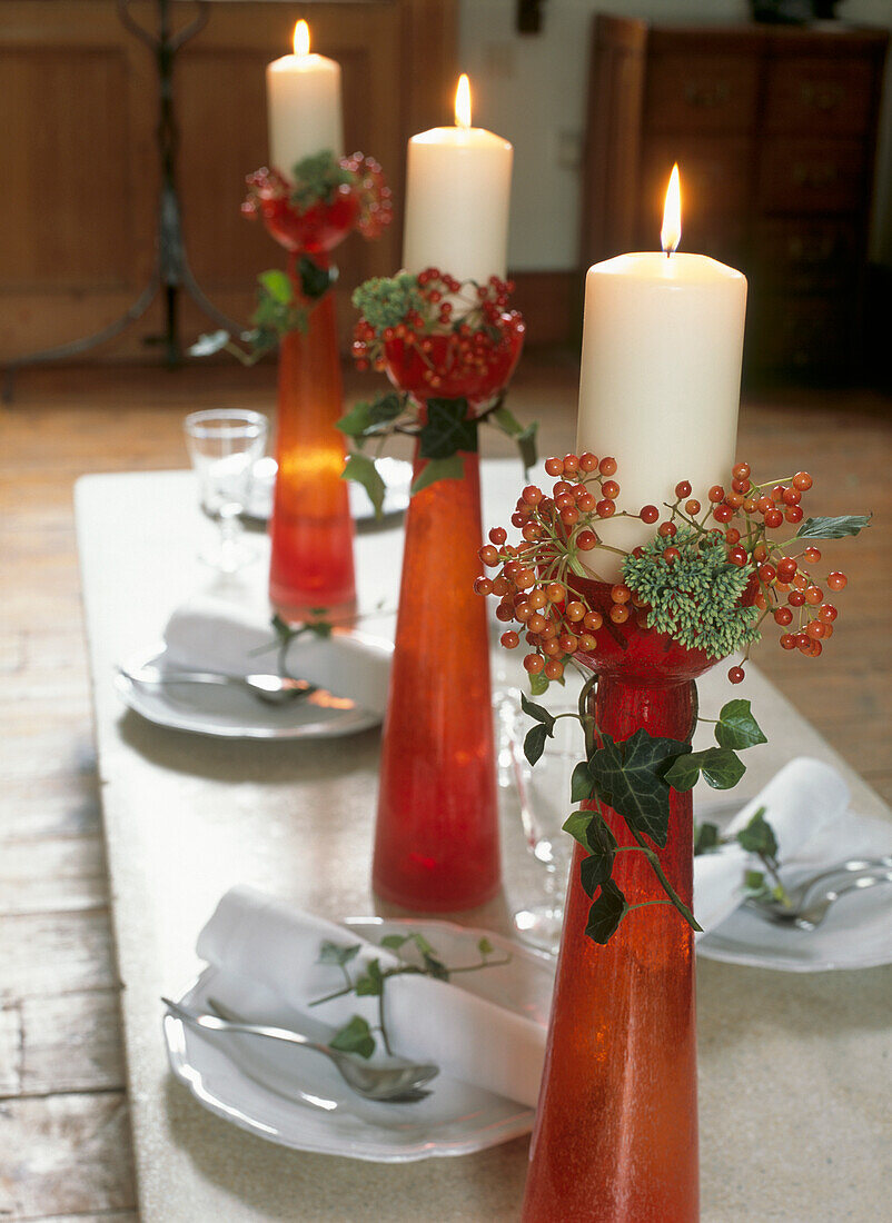 Hübsch gedeckter Wintertisch mit hohen roten Kerzenhaltern und brennenden weißen Kerzen