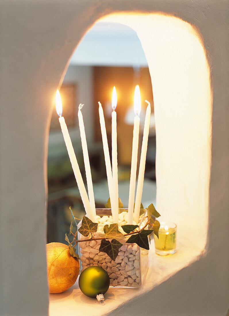 Burning white taper candles in square glass bowl filled with pebbles