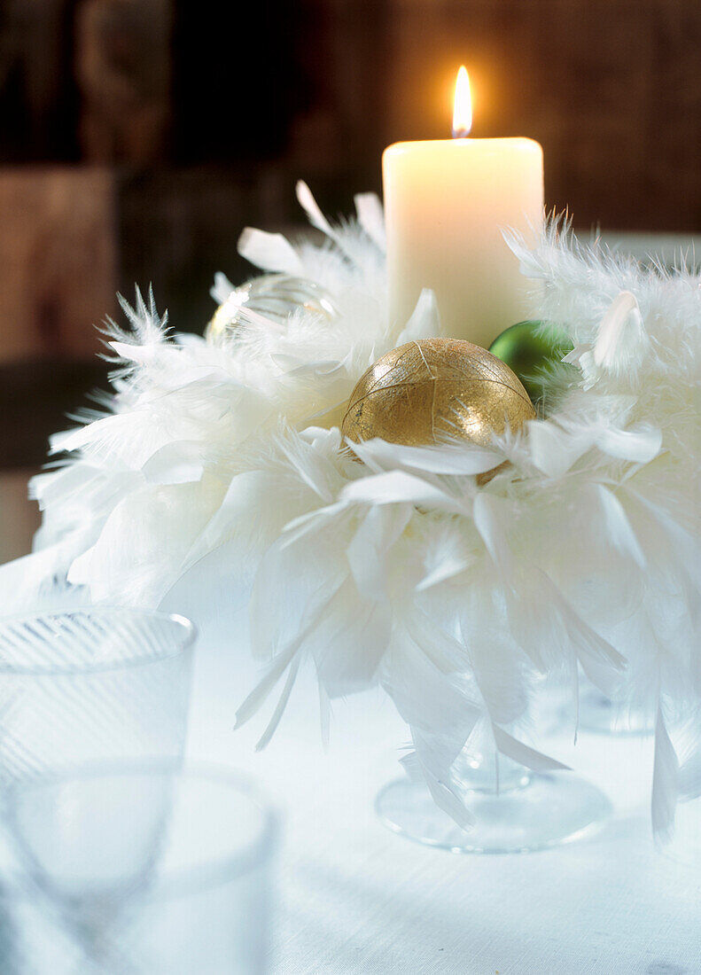 Tafelaufsatz aus weißen Federn und Goldkugeln mit brennender Kerze auf einem Esstisch