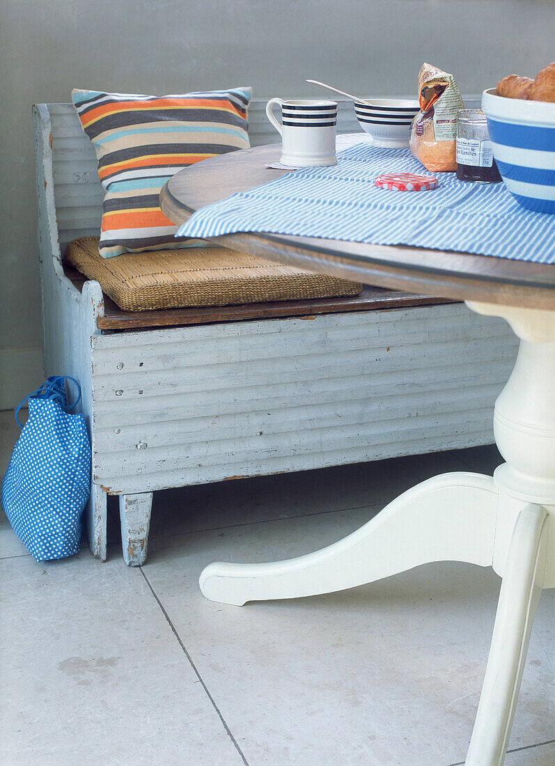 Runder Frühstückstisch mit blassblau gestrichenem, rustikalem Sitz mit gestreiften Polstern