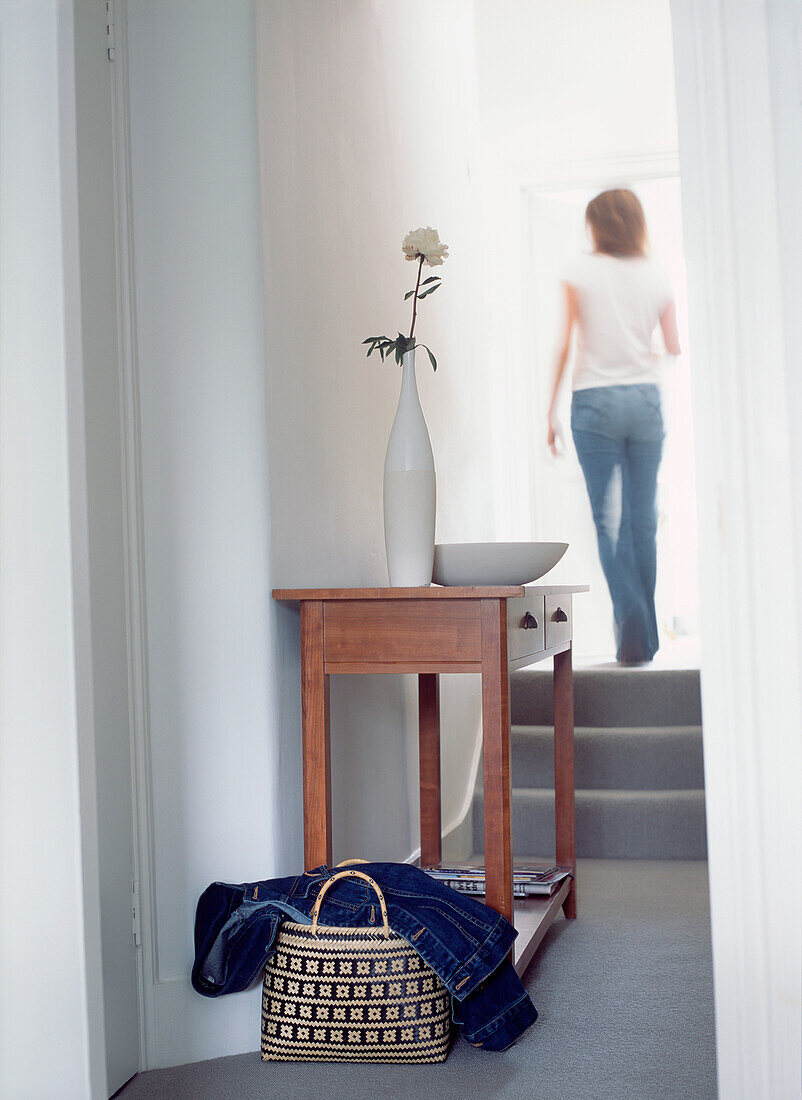 Young woman walking up steps and past wooden console table in hallway 