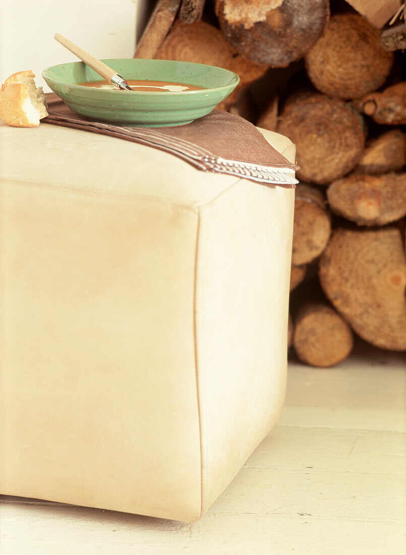 Schüssel mit Suppe und Brot auf einem Fußschemel im Wohnzimmer neben einem Stapel Holzscheite