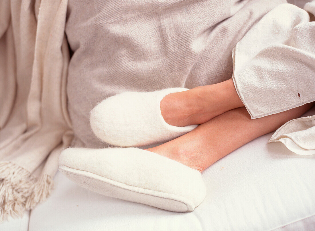 Woman relaxing wearing white felt slippers with her feet up on a comfortable sofa