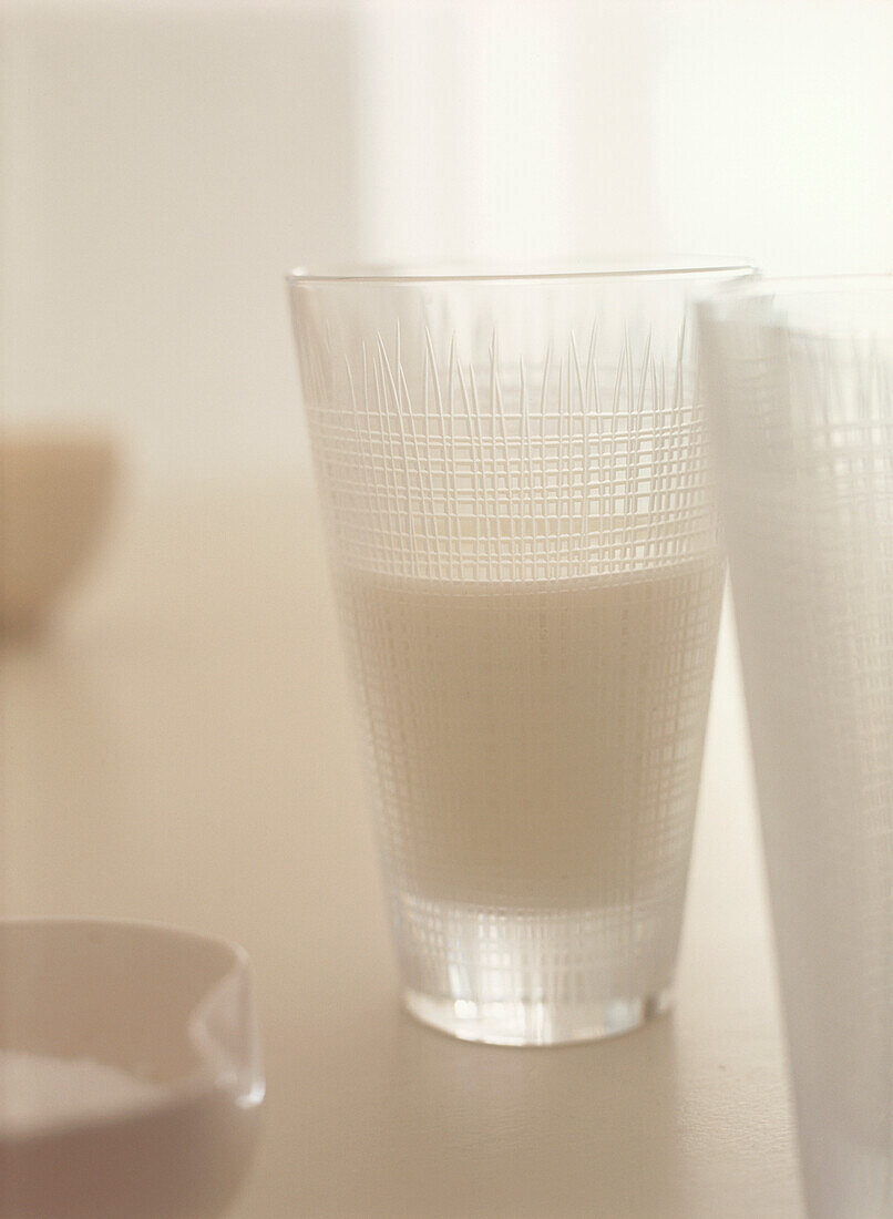 Gläser mit frischer Milch in geätzten Bechern auf einem weißen Küchentisch