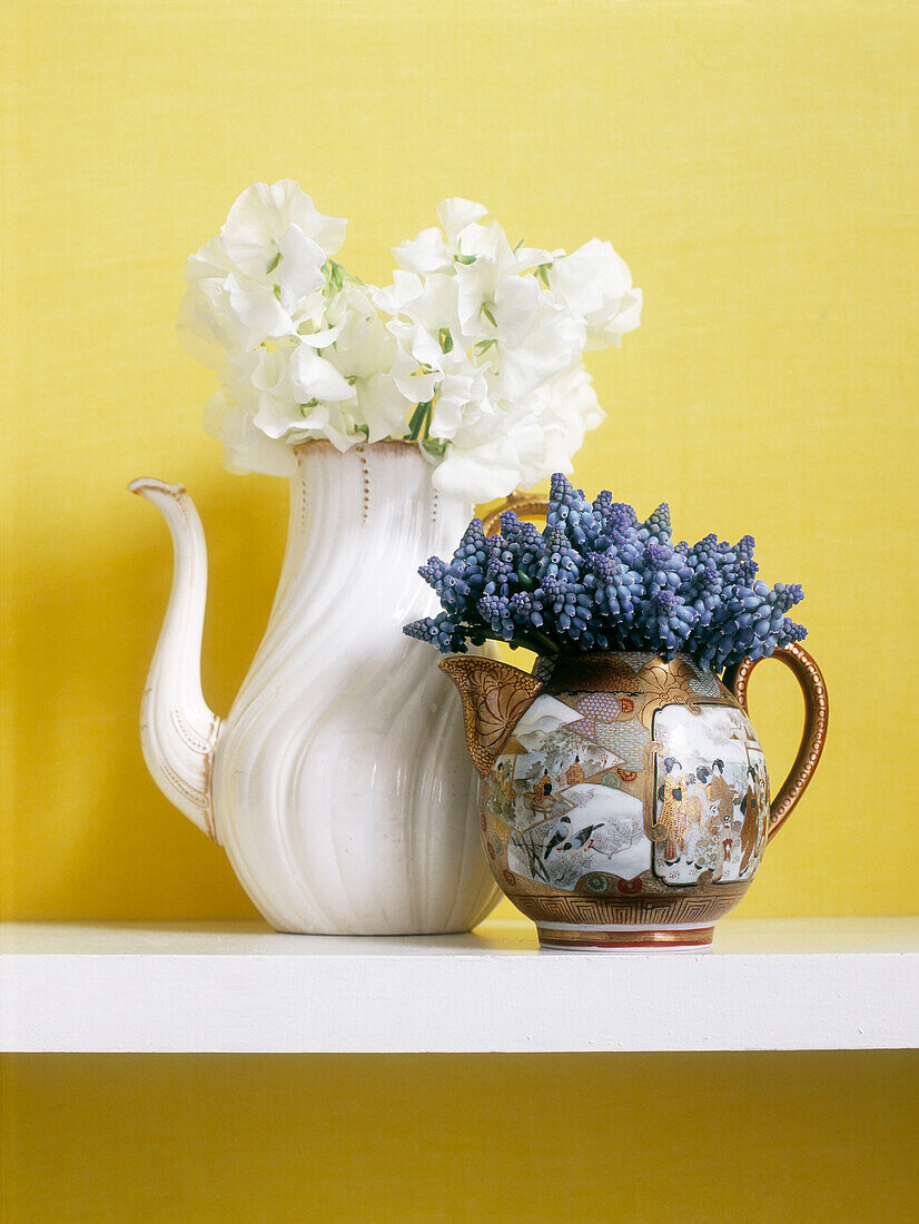 Blaue Hyazinthen in orientalischer Teekanne mit weißem Blumenkübel vor gelber Wand