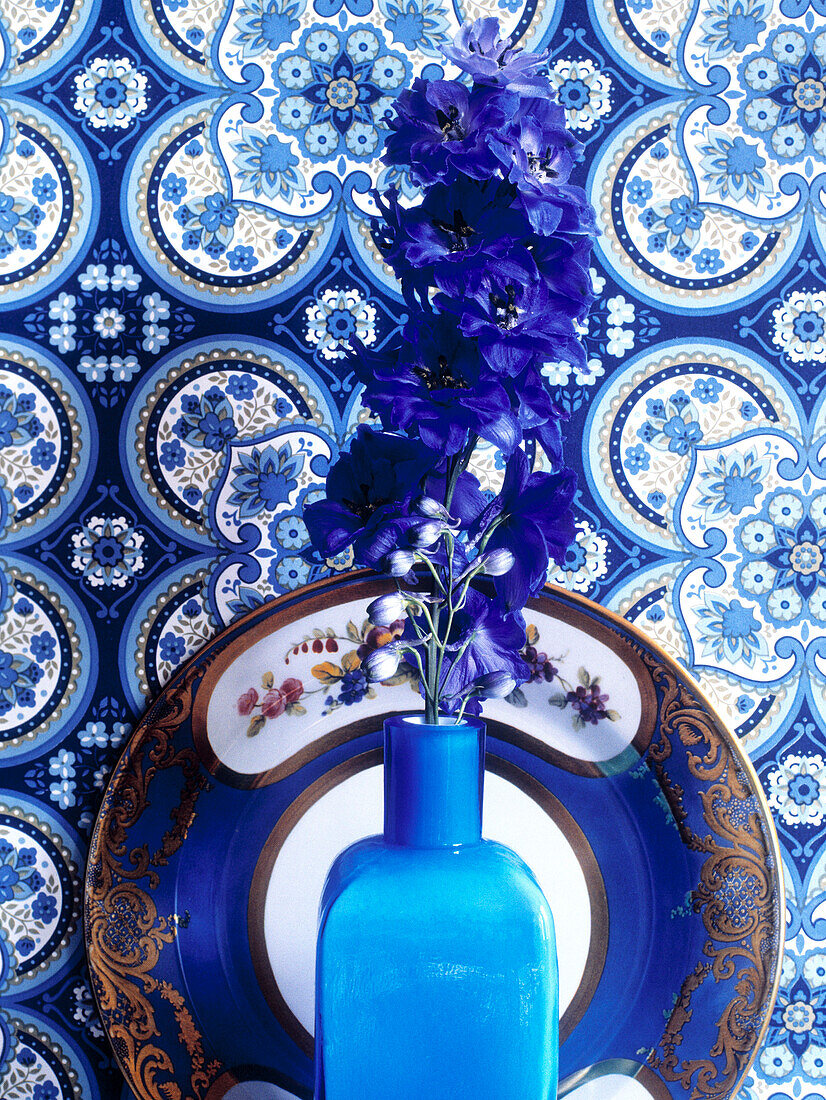 Flowers in vase with blue and white decorative plate and wallpaper