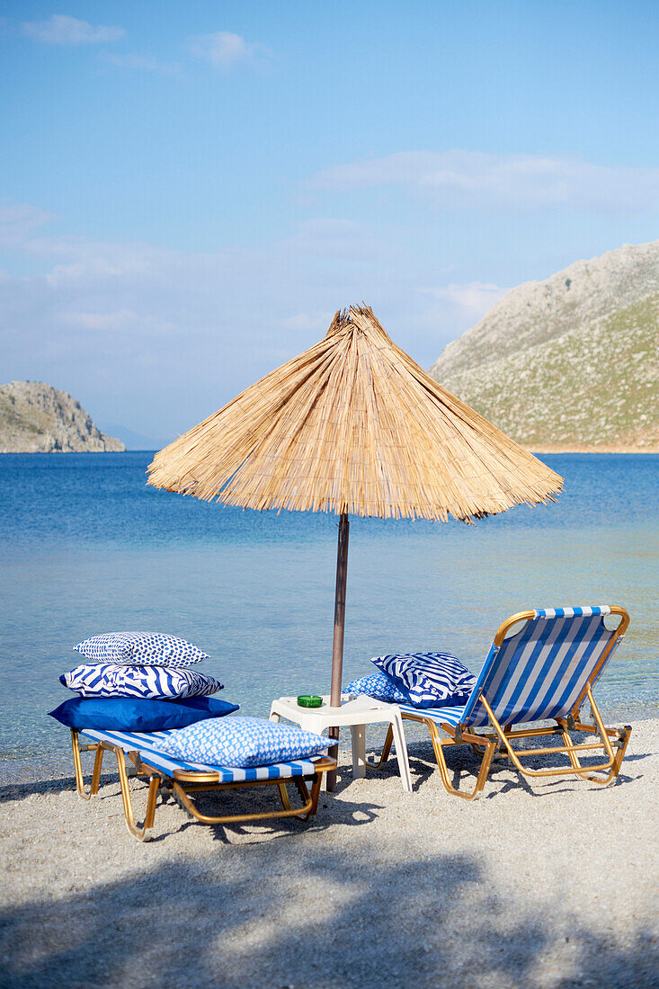 Gestreifte blaue Liegestühle unter Sonnenschirm am griechischen Strand