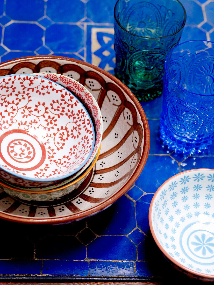 Handbemalte Schalen auf einer blauen Tischplatte mit Gläsern in einem marokkanischen Riad in Nordafrika
