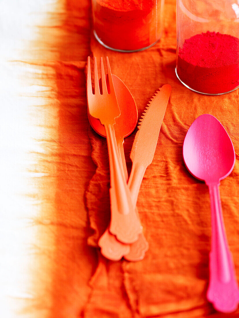 Orange cutlery with pink spoon on tie-dyed fabric with powder